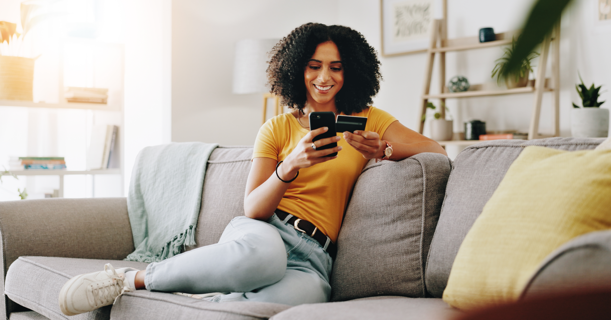 A customer shopping online from her couch with her phone and debit card